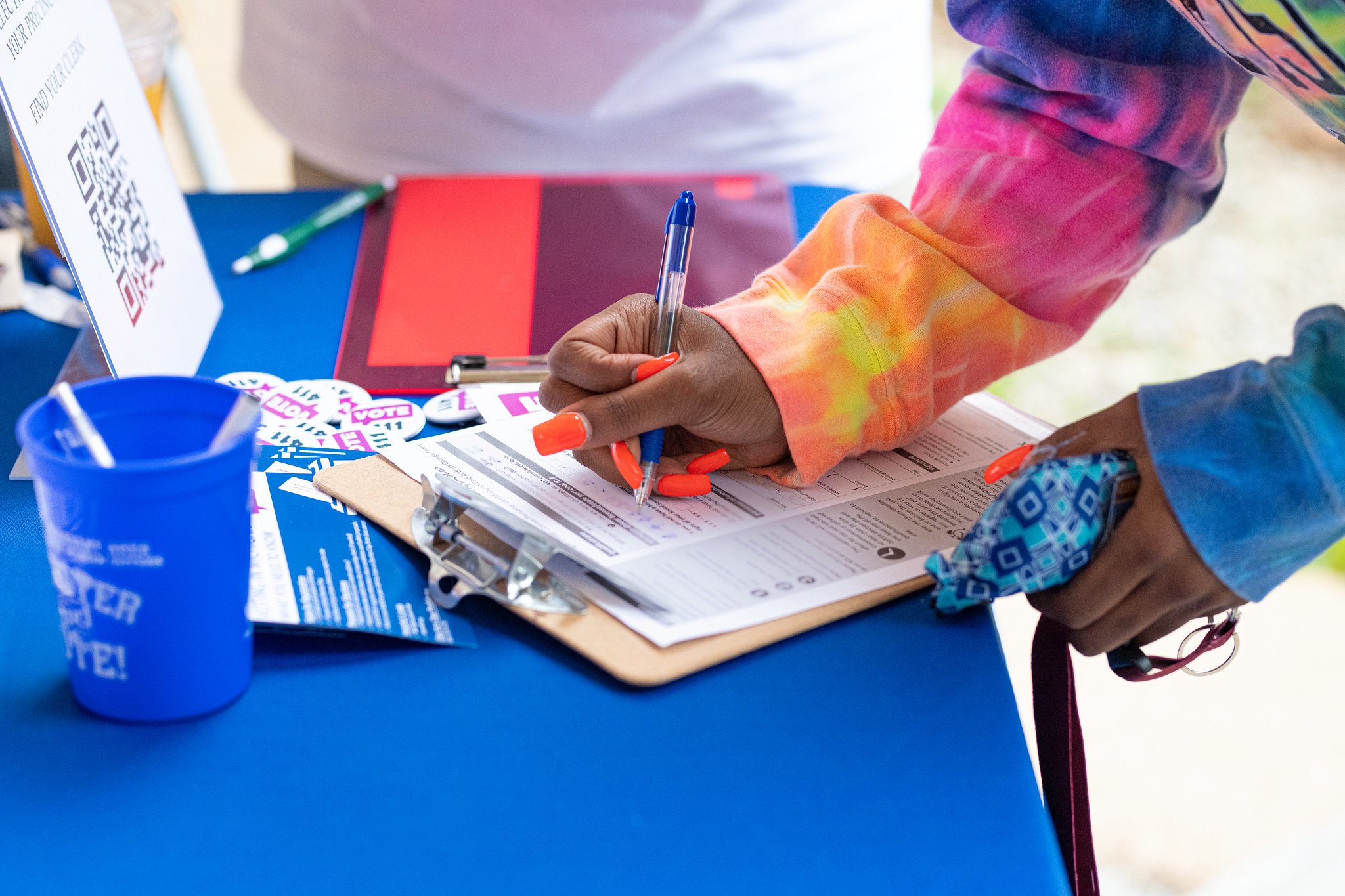 Hand and arm of a young woman with orange fingernails registering to vote