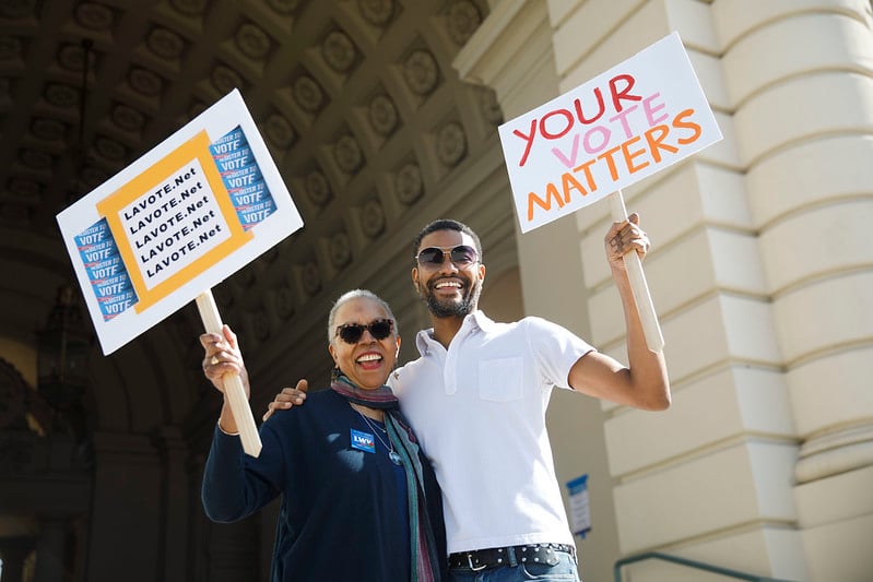 Man and woman holding picket signs that say "Your Vote Matters"