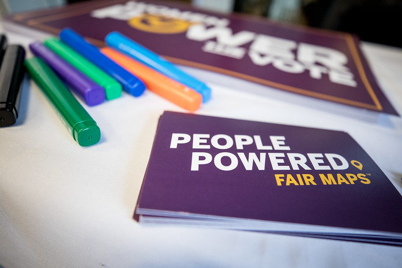 Cards reading "People Powered Fair Maps" on a white tablecloth alongside colorful pens