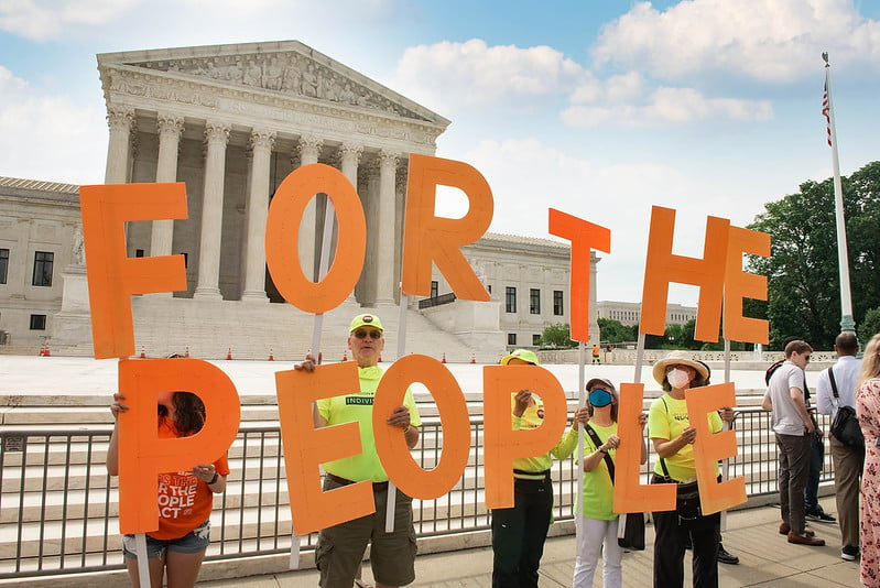 People stand in front of the Capital with letter spelling out "For the People"