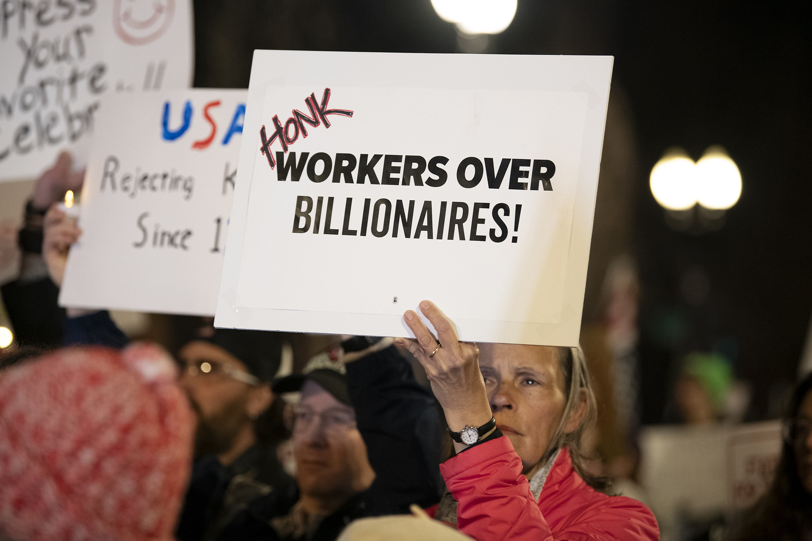 Woman holding a sign that says "honk workers over billionaires"