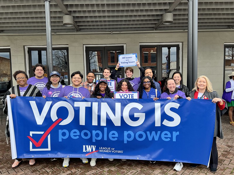 League members holding up a sign that says "Voting is People Power"