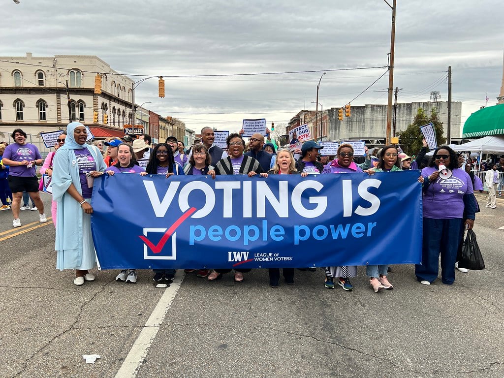 League members holding a "Voting is People Power" banner while marching