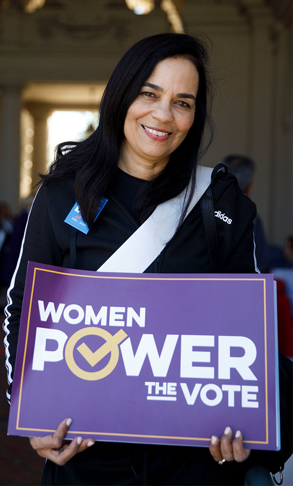 A woman holding a sign that says Women Power the Vote