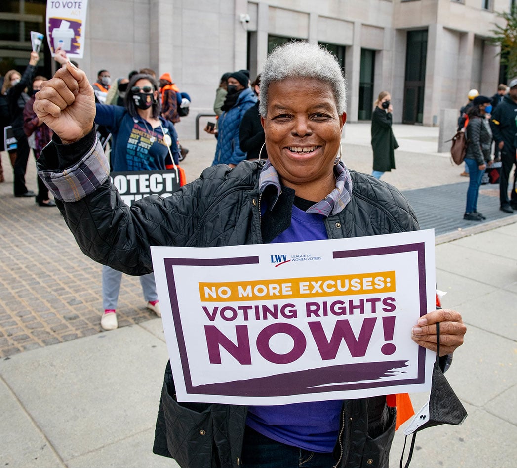 Dr. Turner holding a "Voting Rights Now" sign and raising her fist in solidarity