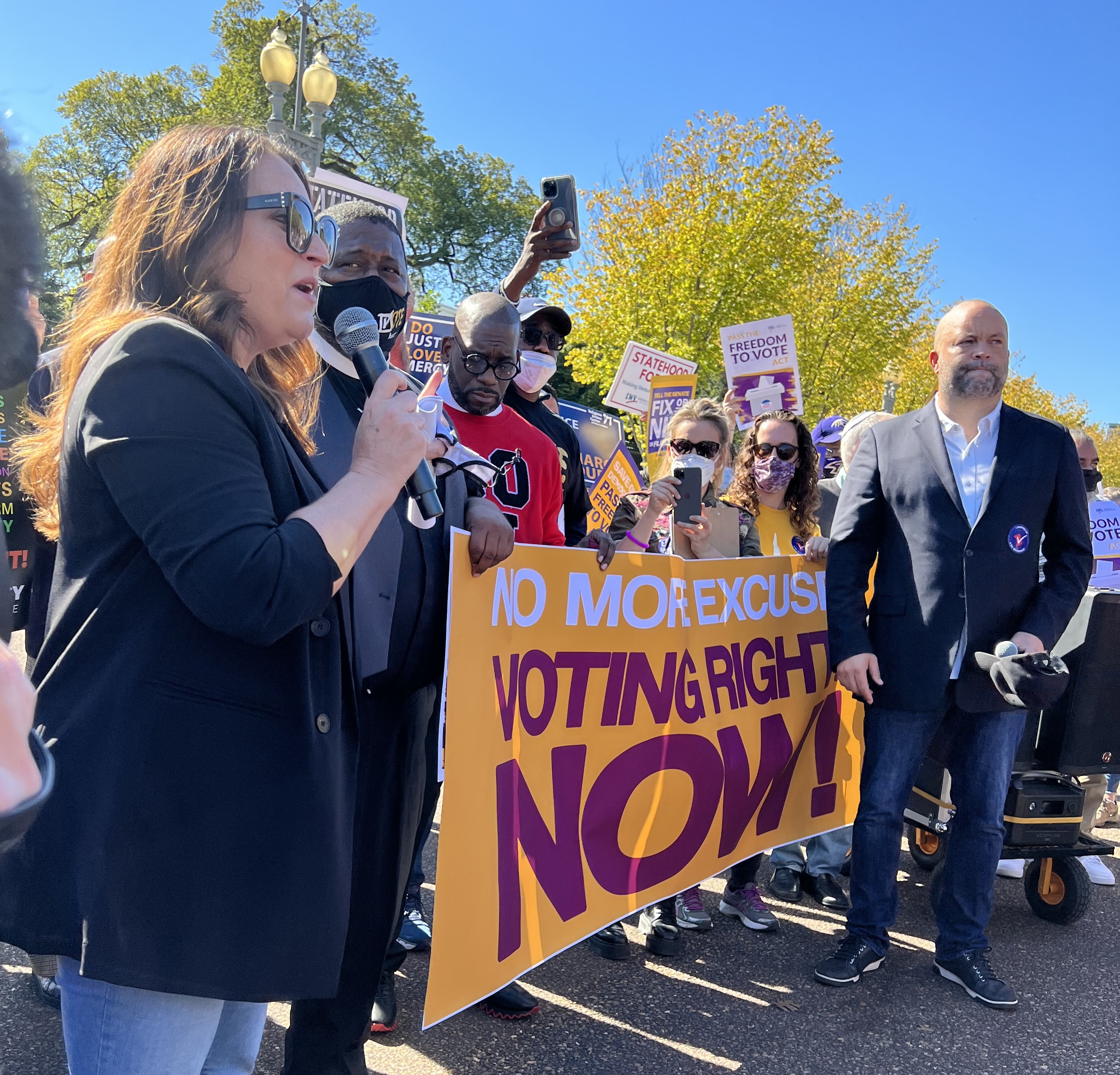 Protestors outdoors holding banner that reads "Voting Rights NOW!"