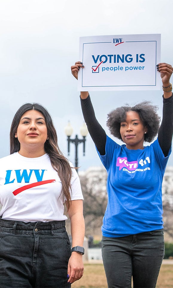 League members standing outside, one holding a sign that says "Voting is People Powered"