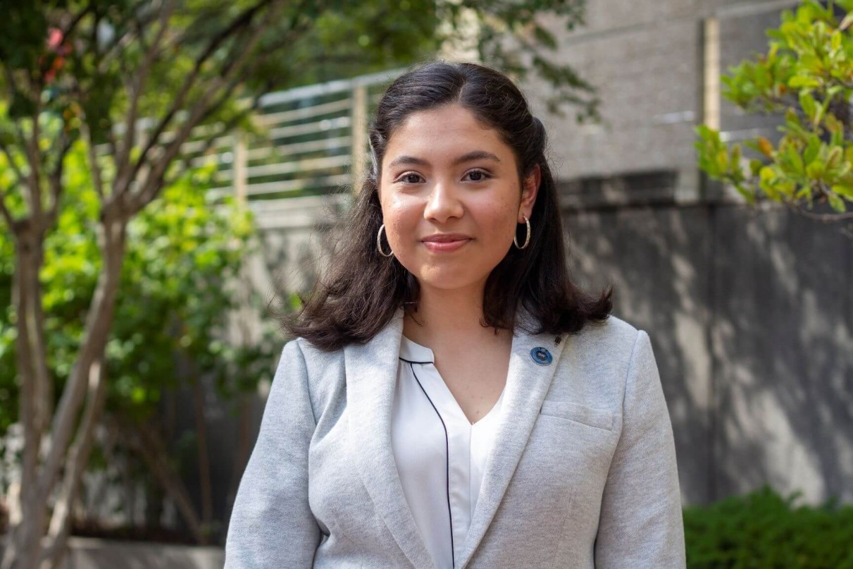 Woman in gray suit in front of leafy background