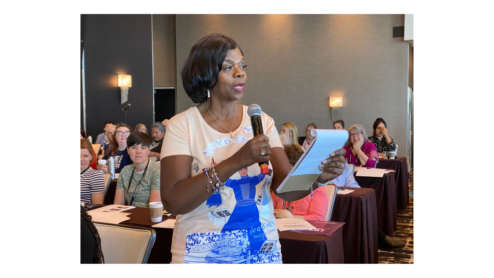 Attendee speaking during Friday's exercise: a game of telephone! They are holding a microphone and a pad of paper.