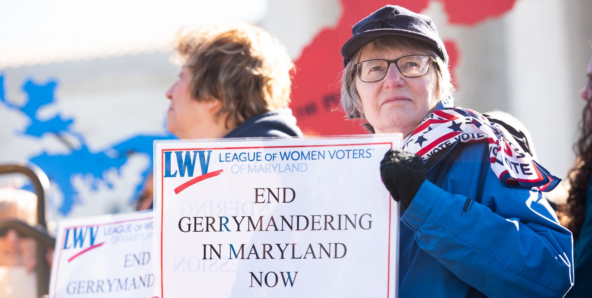 Woman outdoors at rally holding sign that reads "End Gerrymandering in Maryland Now"