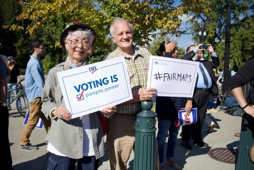 Two people standing side by side holding signs promoting fair maps
