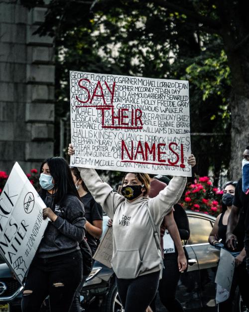 A woman holding a sign that says "Say Their Names" with the names of Black people lost to police brutality