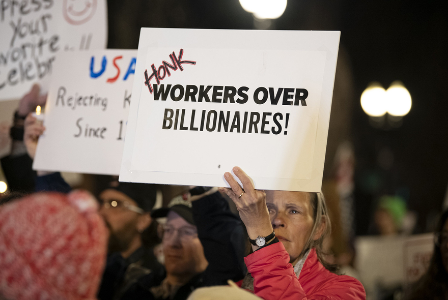 Woman holding a sign that says "honk workers over billionaires"