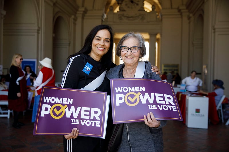 Two women holding signs saying "Women Power the Vote"