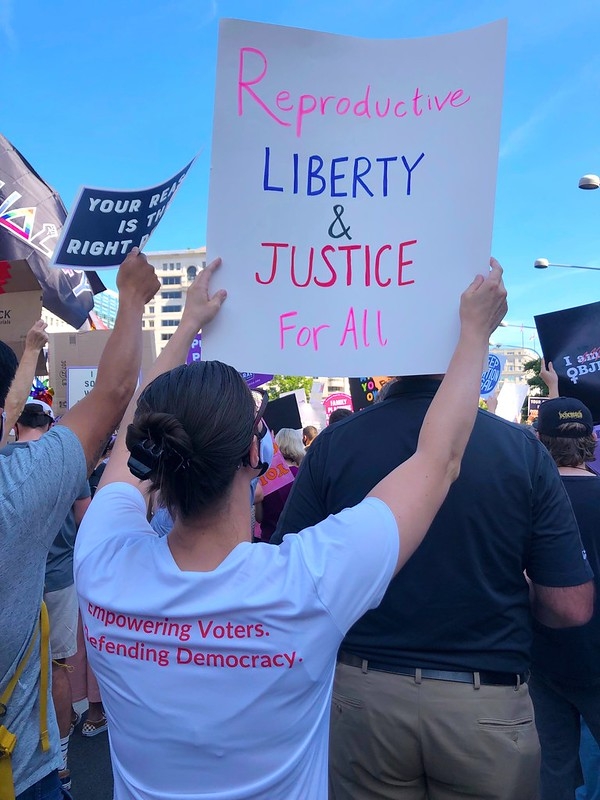 A League member holding a sign that says "Reproductive liberty and justice for all."