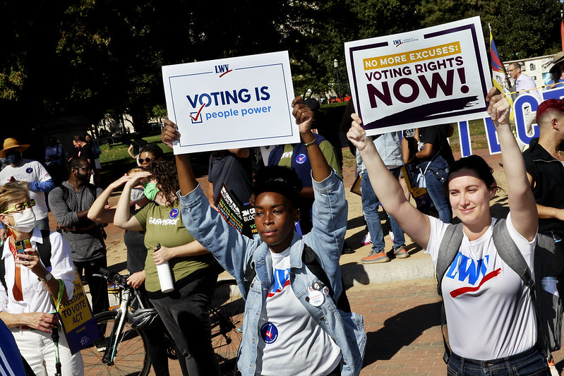 League members holding signs that say "Voting is People Power" and "Voting Rights Now" at a rally