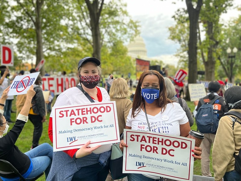 Two people in masks holding signs that say "Statehood for DC"