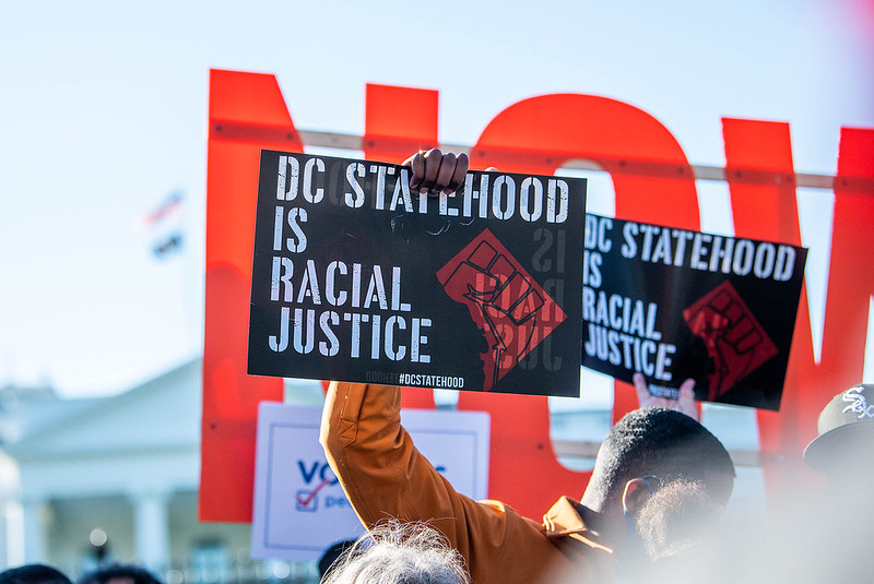 A man holding up a sign that says "DC Statehood is Racial Justice"