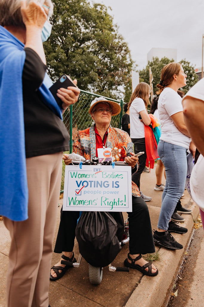 An LWV member in a wheelchair holding a sign that says "Women's Bodies, Women's Rights"