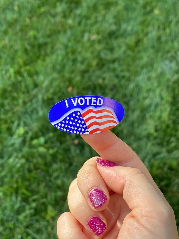 A hand with sparkly pink nails holding up an "I Voted" sticker