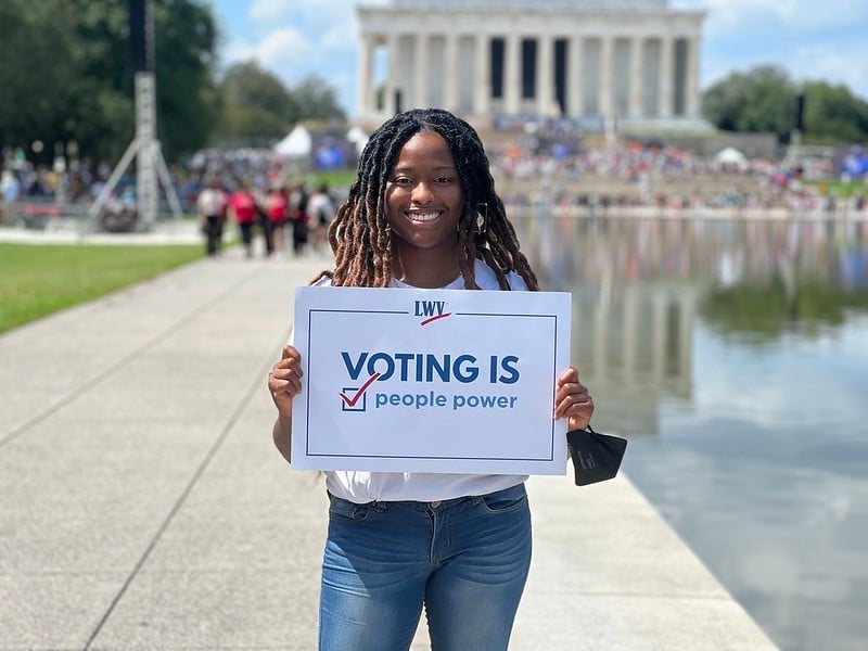 A LWV member holding a sign in front of the Lincoln Memorial that says "Voting is People Powered"