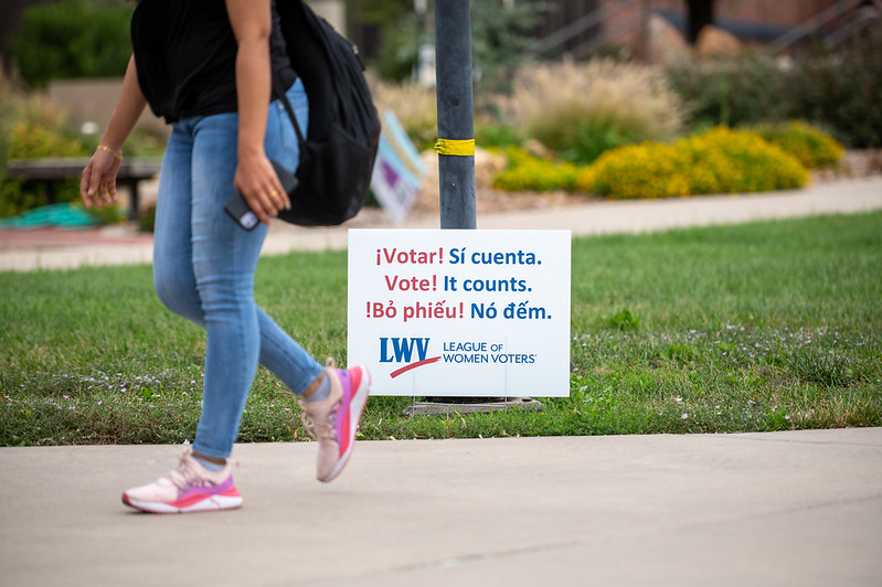 Person walking past a voting sign that says "Vote! It counts" in many languages