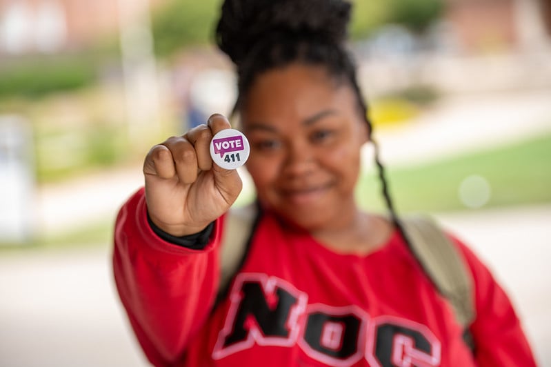 A young woman in a red sweatshirt holding a VOTE411 pin