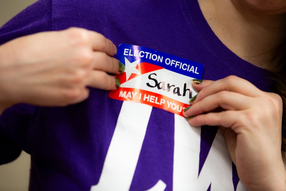 A person in a purple LWV short putting on an election official badge that says "My name is Sarah"
