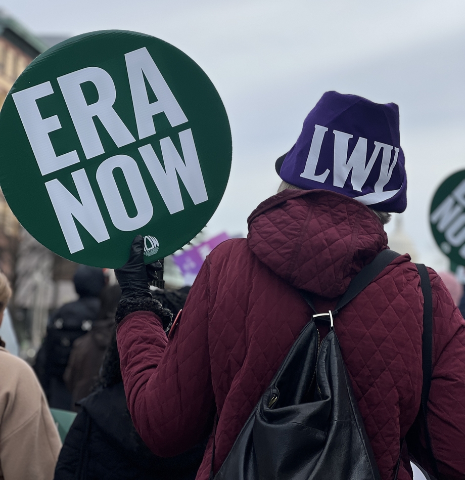 A person in an LWV hat holding a sign that says "ERA Now"