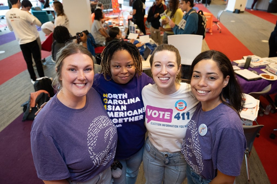 Four women smiling at a voter registration event, one is wearing a VOTE411 t-shirt