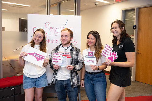 Four people holding signs encouraging voting and voter registration and smiling
