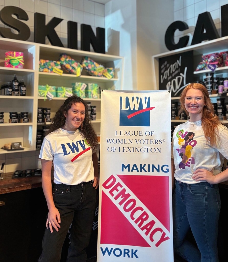 Two League members in front of a League banner in a LUSH store