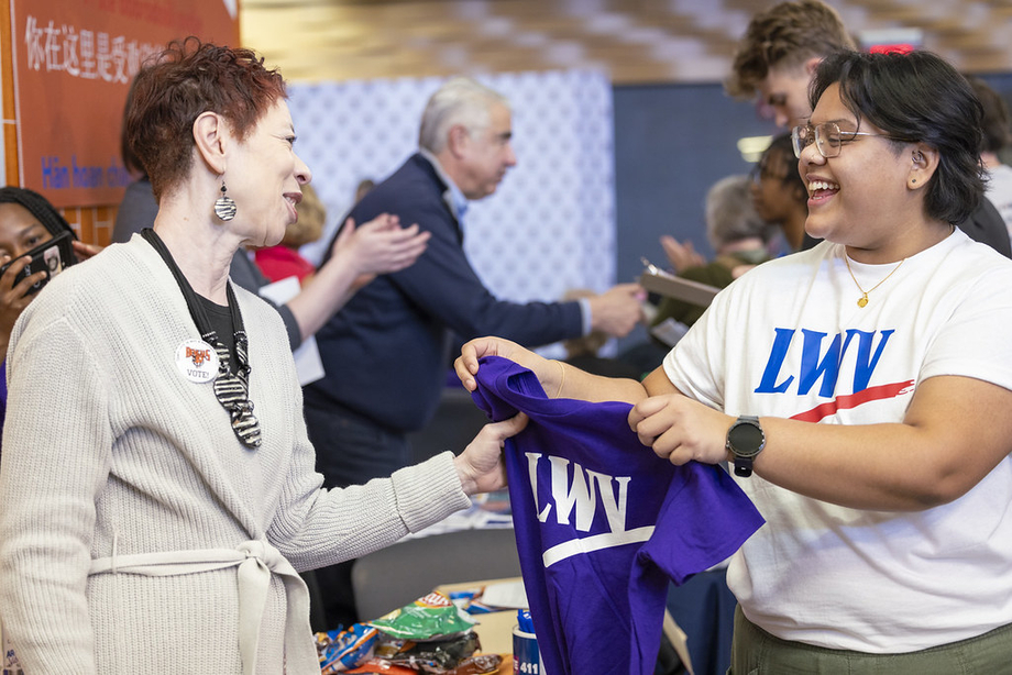 An LWV member handing out an "LWV" shirt at a registration event