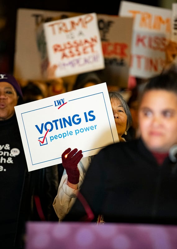 A woman holding a sign that says "Voting is People Power" 
