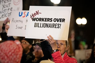 A protestor holding a sign that says "HONK Workers Over Billionaires"