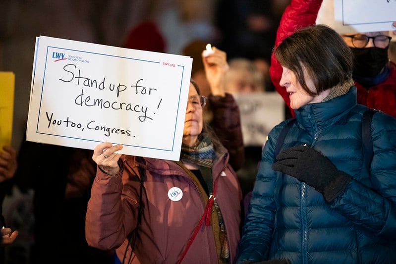 Two women, one holding a sign that says "Stand Up for Democracy -- You Too, Congress"