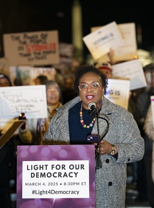 CEO Celina Stewart speaking at a podium in front of a rally crowd