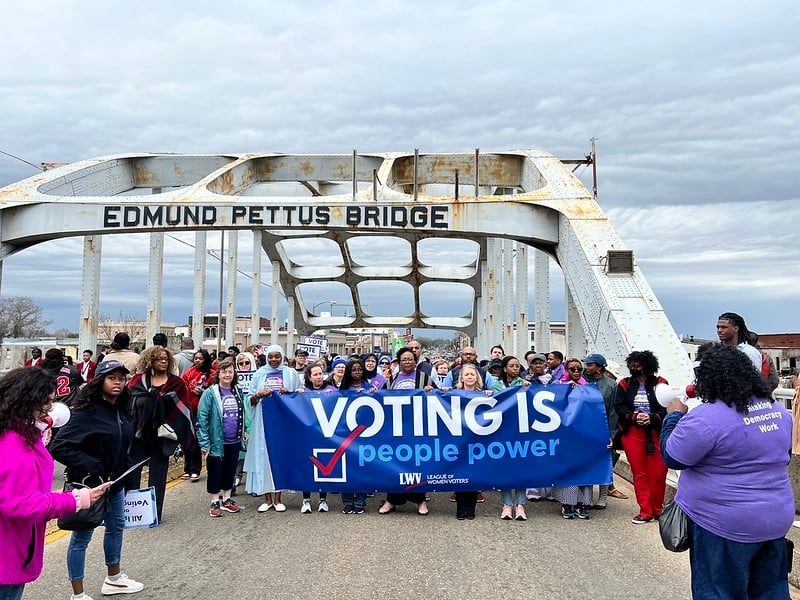 League members holding a "Voting is People Power" sign on the Edmund Pettus bridge