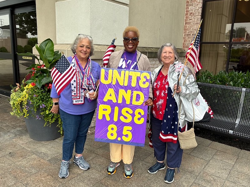 Chief Counsel Marcia Johnson holding a sign that says "Unite and Rise 8.5" with women on either side of her