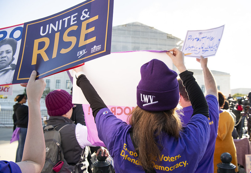 A League member protesting in front of the Supreme Court next to someone holding a Unite and Rise sign