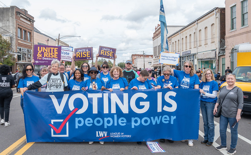 League members holding a banner that says "Voting is People Power" and many "Unite and Rise" signs
