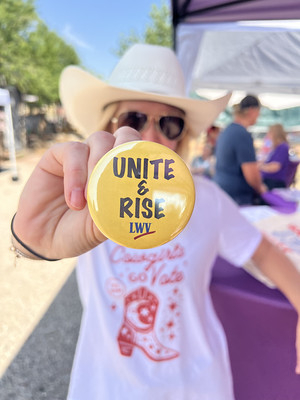 A person in a cowboy hat holding a "Unite and Rise" pin