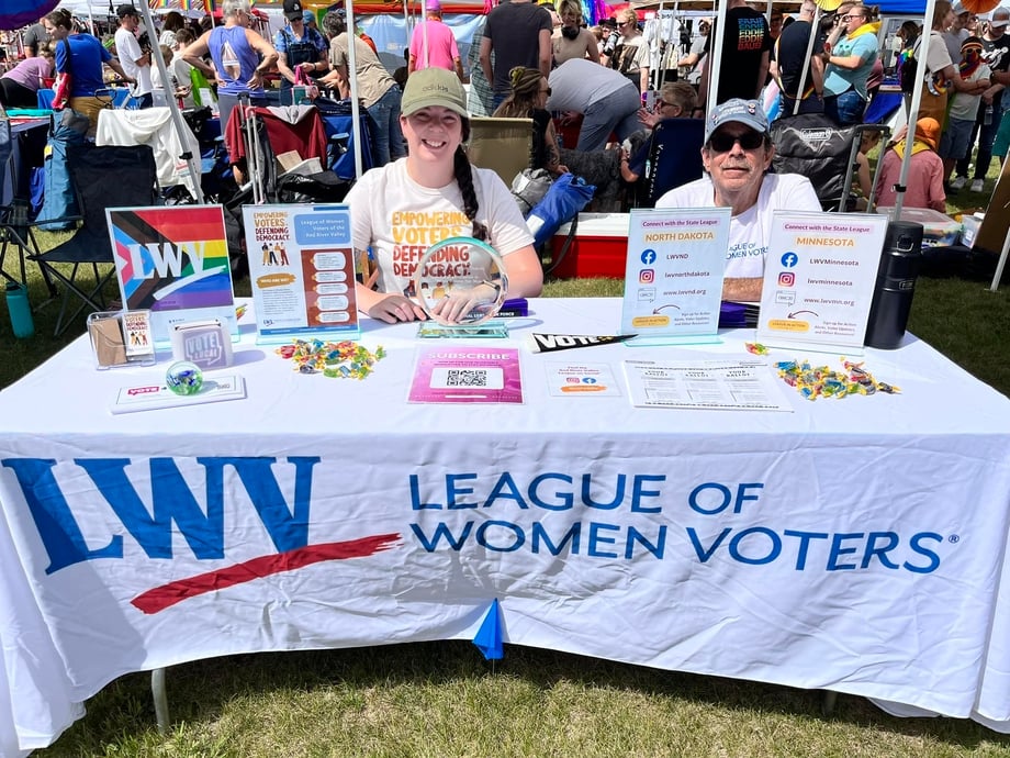 League members sitting at a table with an LWV banner during a Pride event