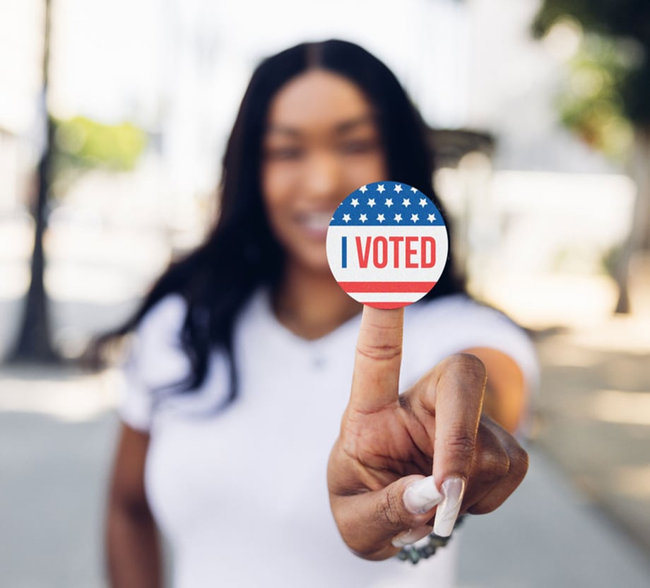 A woman holding up an "I Voted" sticker