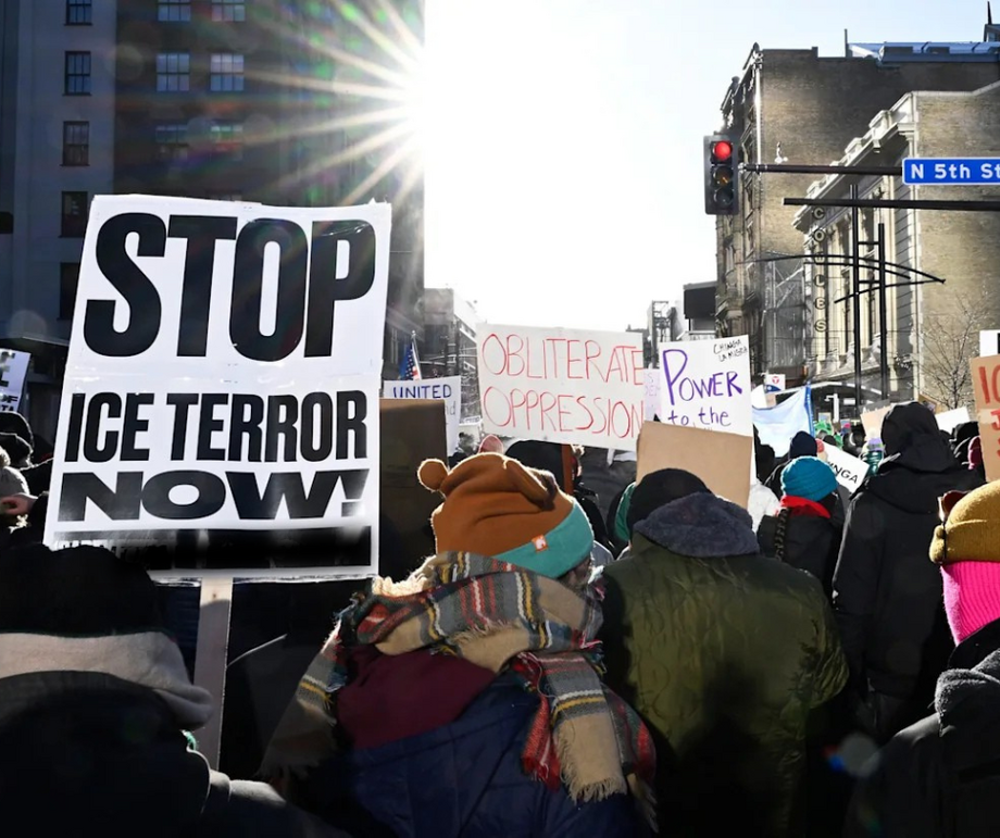 A crowd of protestors, one holding a sign that says "Stop ICE Terror Now"