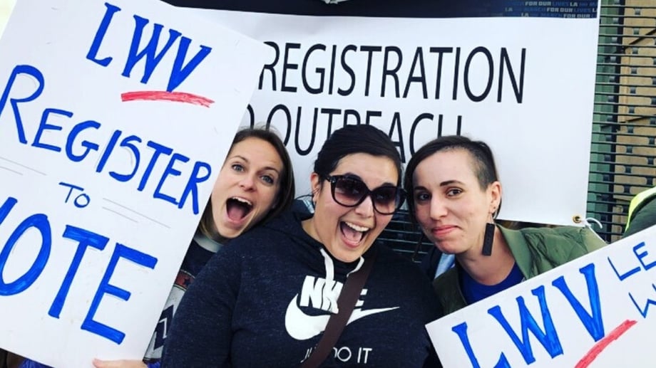Three women holding LWV Register to VOTE signs at Registration Event
