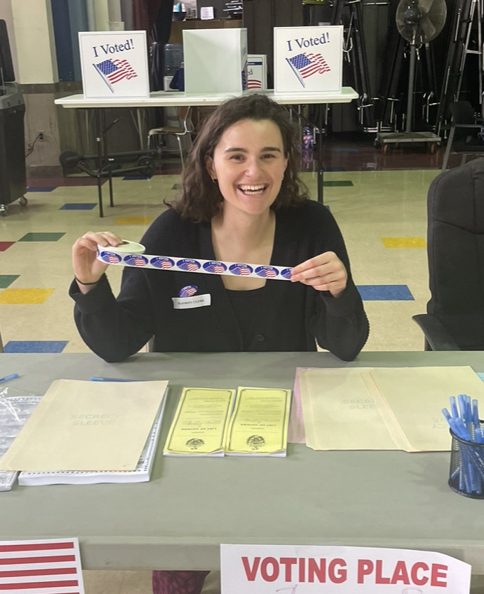 Communications specialist Mary Roche holding up "I voted" stickers while volunteering at a local election