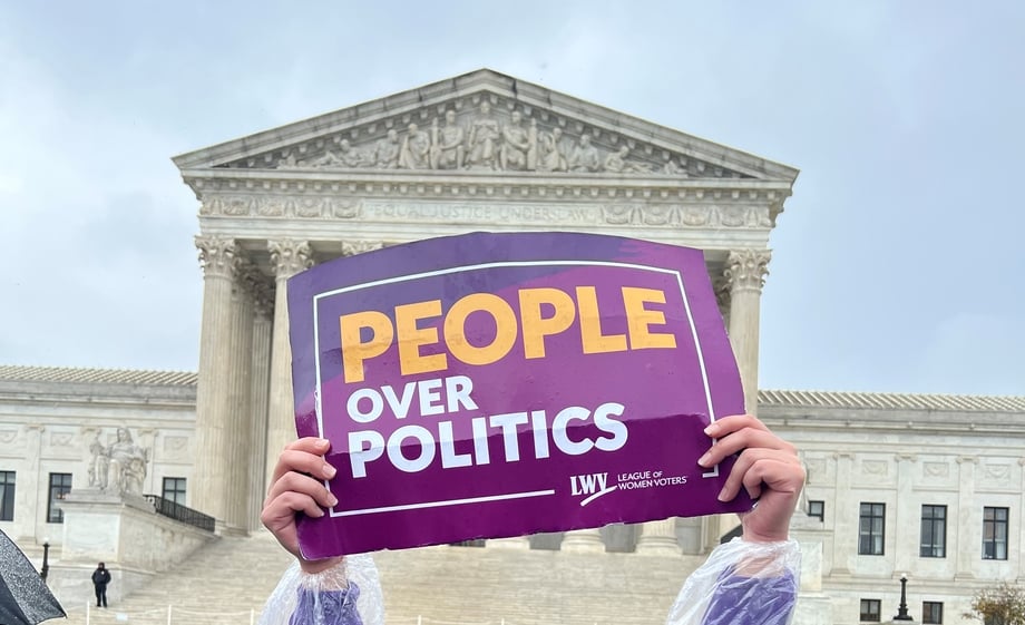 Hands holding purple and gold sign that reads "PEOPLE OVER POLITICS" in front of the US Supreme Court Building