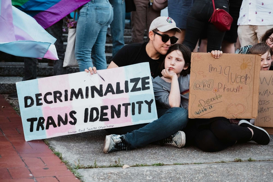 A parent and child holding a sign that says "decriminalize trans identity"