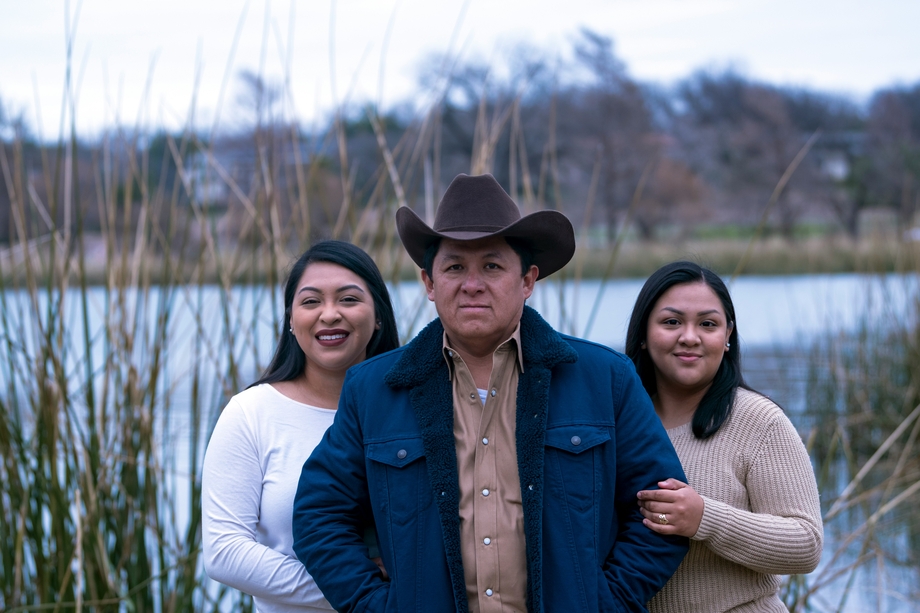 Three Native people standing in front of a lake and smiling
